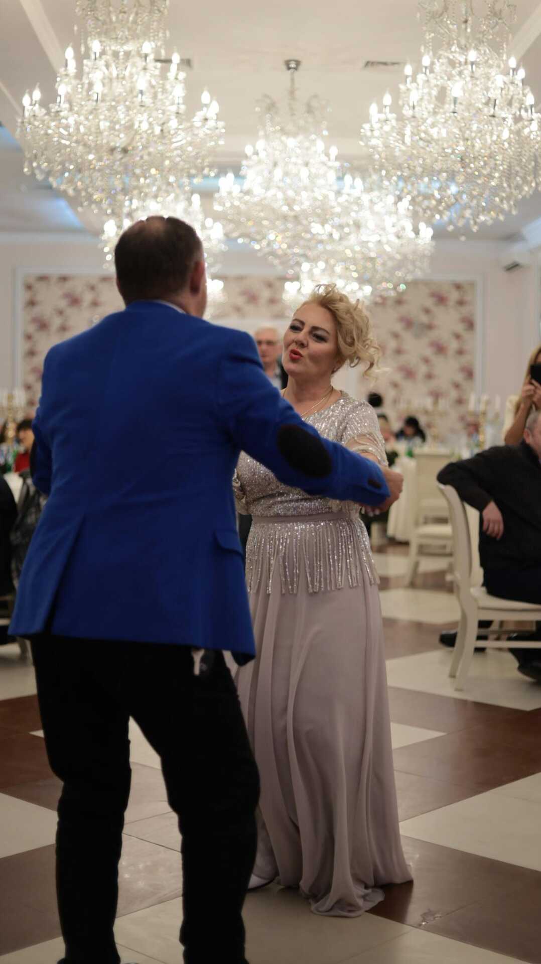 A couple elegantly dancing at a glamorous reception with chandeliers overhead.