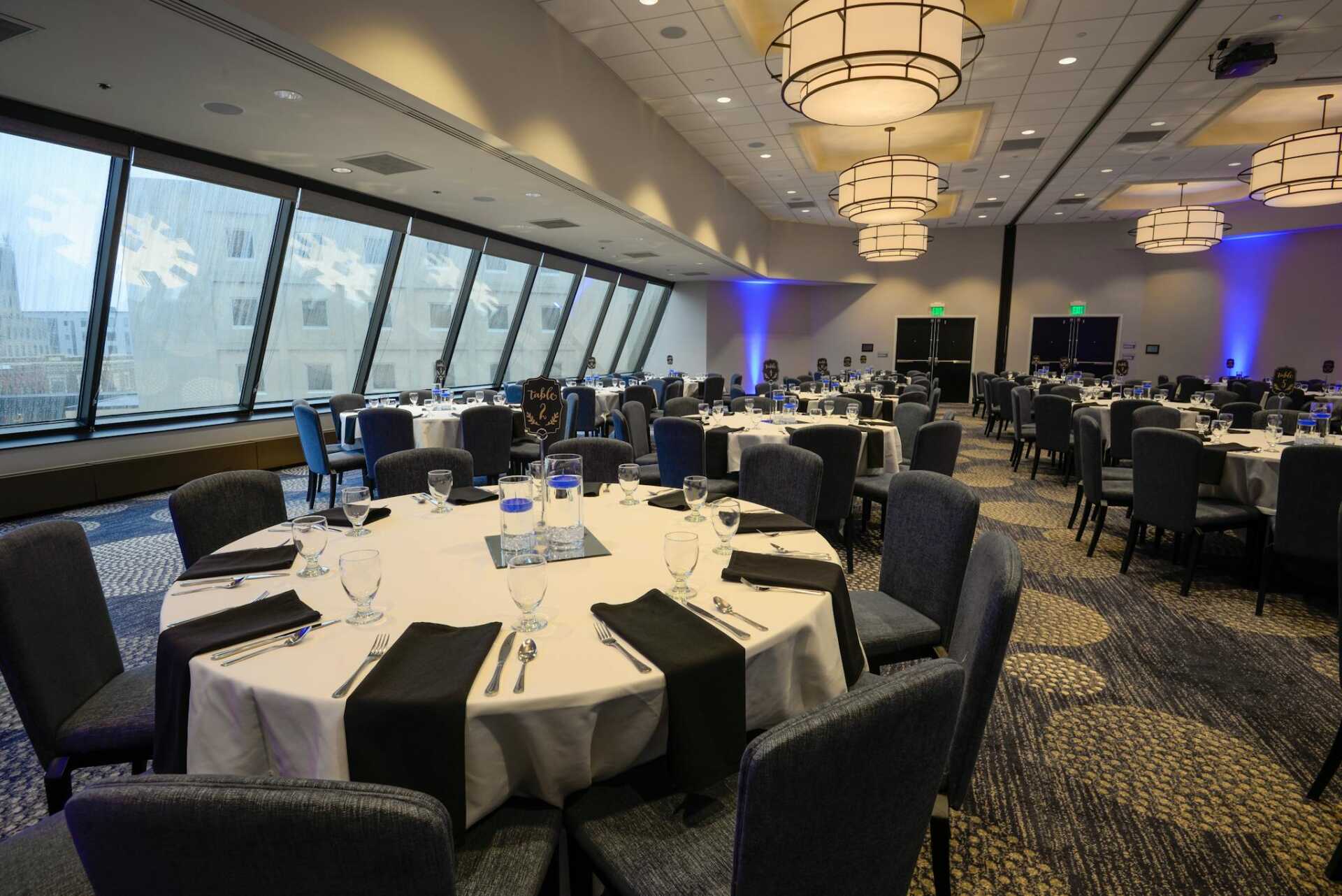 Spacious banquet hall with elegantly set round tables and modern interior lighting.